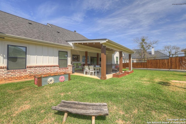 back of property with a lawn, fence, board and batten siding, a shingled roof, and a patio area