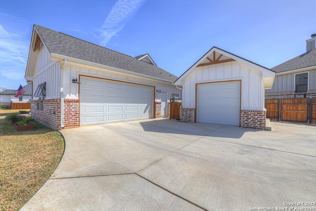 view of front of house with brick siding, board and batten siding, a detached garage, fence, and roof with shingles