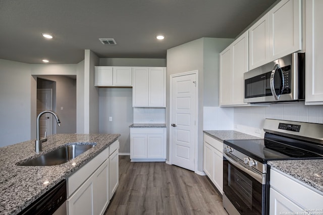 kitchen featuring visible vents, appliances with stainless steel finishes, wood finished floors, white cabinets, and a sink