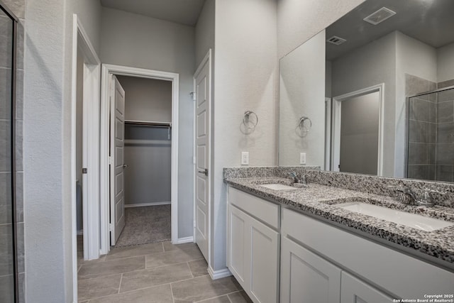 full bath with a spacious closet, tiled shower, visible vents, and a sink