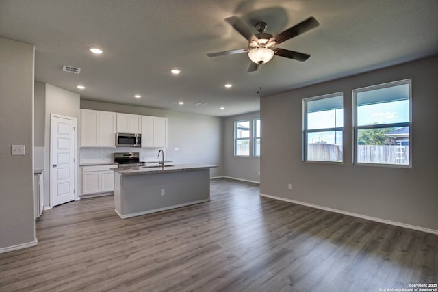 kitchen with wood finished floors, a sink, stainless steel appliances, white cabinetry, and open floor plan