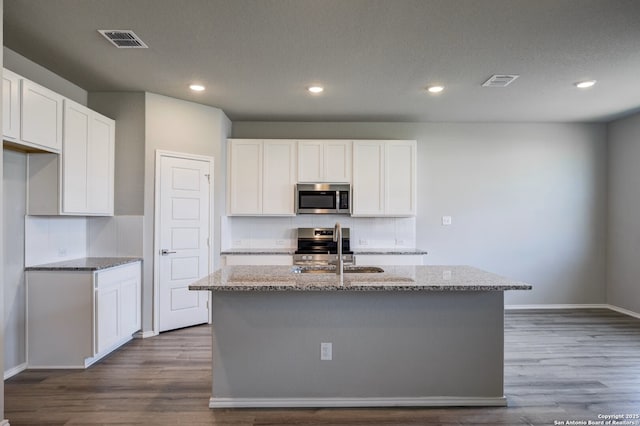 kitchen featuring dark wood-type flooring, light stone countertops, visible vents, and stainless steel appliances