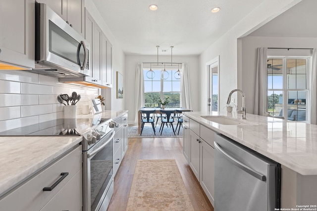 kitchen with light wood-style flooring, a sink, light stone counters, tasteful backsplash, and stainless steel appliances