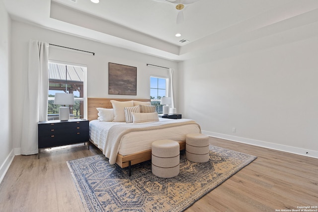 bedroom with a tray ceiling, multiple windows, wood finished floors, and baseboards