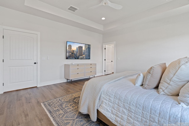 bedroom with wood finished floors, visible vents, baseboards, recessed lighting, and a raised ceiling