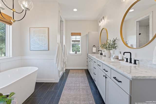 full bath featuring a freestanding bath, double vanity, wainscoting, and a sink