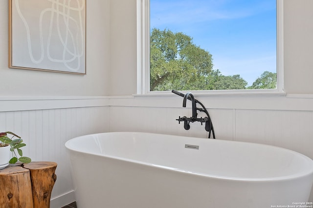 full bath featuring a freestanding tub, a wainscoted wall, and a wealth of natural light