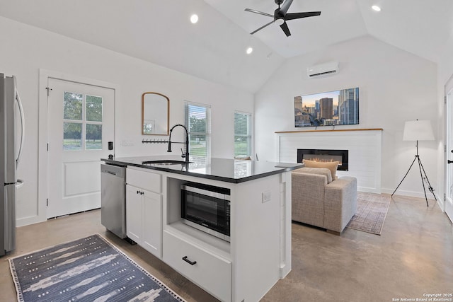 kitchen with an AC wall unit, a sink, dark countertops, a glass covered fireplace, and appliances with stainless steel finishes