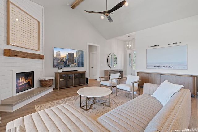 living room with wood finished floors, high vaulted ceiling, beamed ceiling, ceiling fan with notable chandelier, and a large fireplace