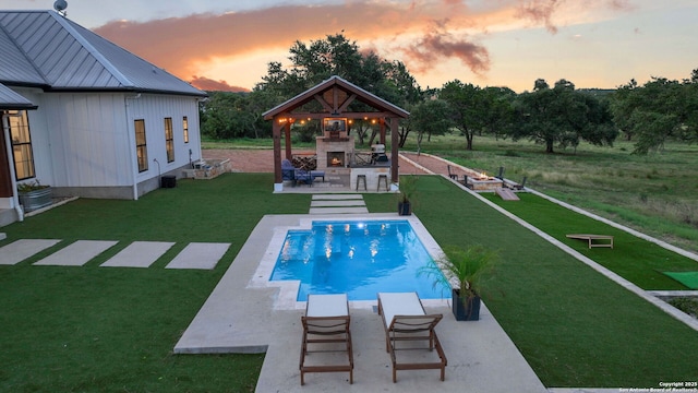 outdoor pool with a gazebo, a yard, a patio area, and an outdoor stone fireplace