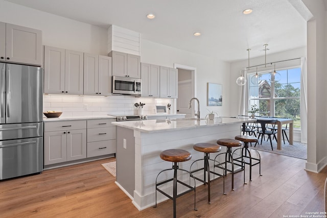 kitchen featuring tasteful backsplash, light wood finished floors, gray cabinetry, and stainless steel appliances