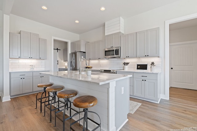 kitchen featuring a sink, appliances with stainless steel finishes, a kitchen breakfast bar, light wood-style floors, and a kitchen island with sink