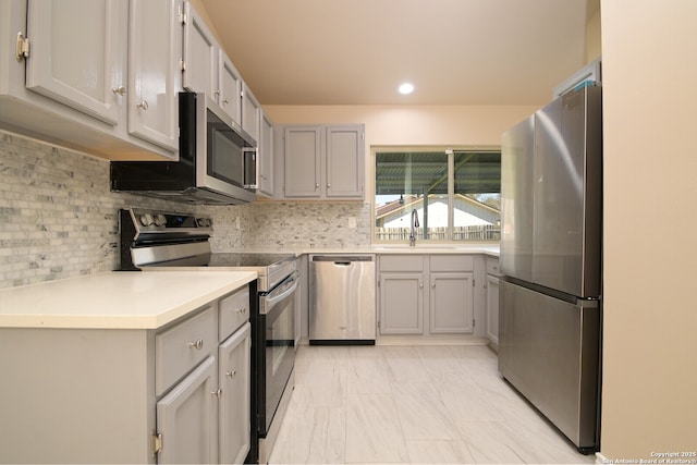 kitchen with decorative backsplash, appliances with stainless steel finishes, gray cabinetry, and a sink