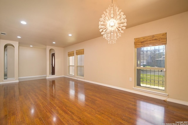 spare room featuring a chandelier, a healthy amount of sunlight, and hardwood / wood-style flooring