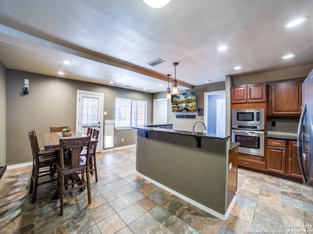 kitchen with visible vents, an island with sink, a sink, stainless steel appliances, and baseboards