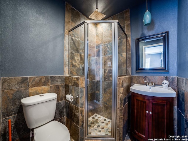 bathroom with toilet, tile walls, a stall shower, and vanity