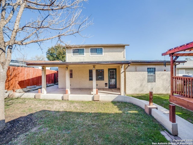 rear view of property with stucco siding, a lawn, a patio, and fence