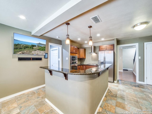 kitchen with visible vents, dark stone counters, appliances with stainless steel finishes, wall chimney range hood, and brown cabinets