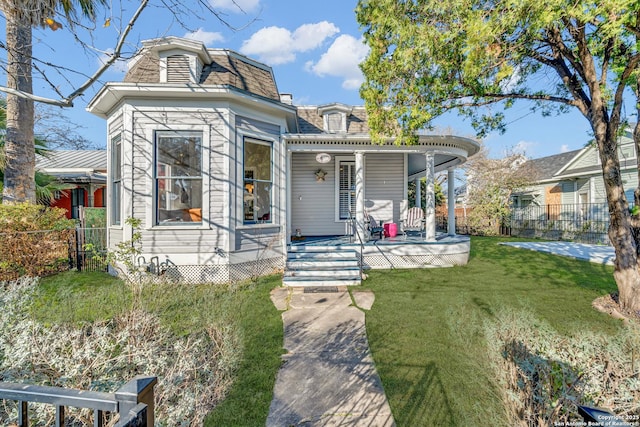 second empire-style home with covered porch, mansard roof, a front yard, and fence