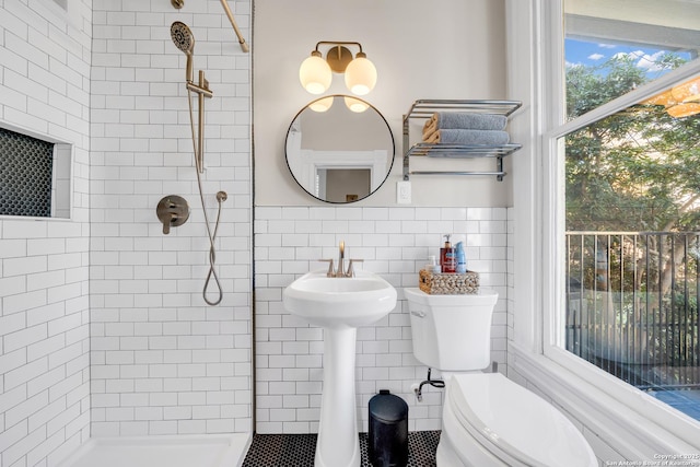 full bathroom with tiled shower, wainscoting, toilet, and tile walls