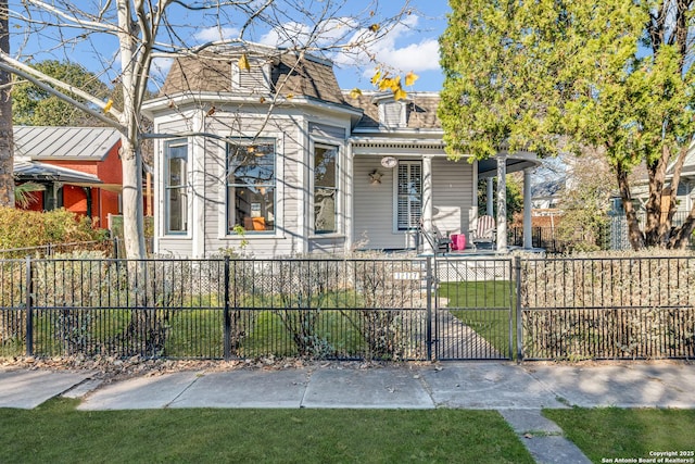 second empire-style home featuring a front lawn, mansard roof, and a fenced front yard