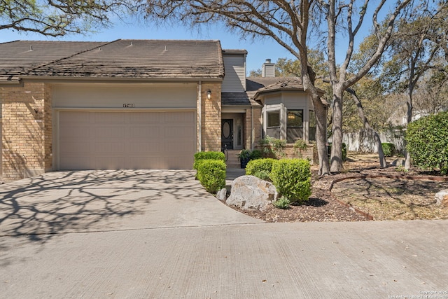 view of front facade featuring brick siding, an attached garage, concrete driveway, and a chimney