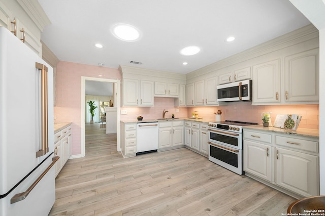 kitchen featuring white appliances, light wood-style flooring, recessed lighting, a sink, and backsplash