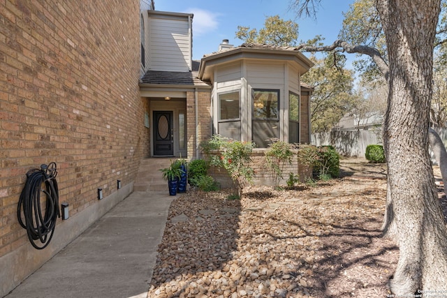 view of exterior entry with crawl space, brick siding, and a chimney