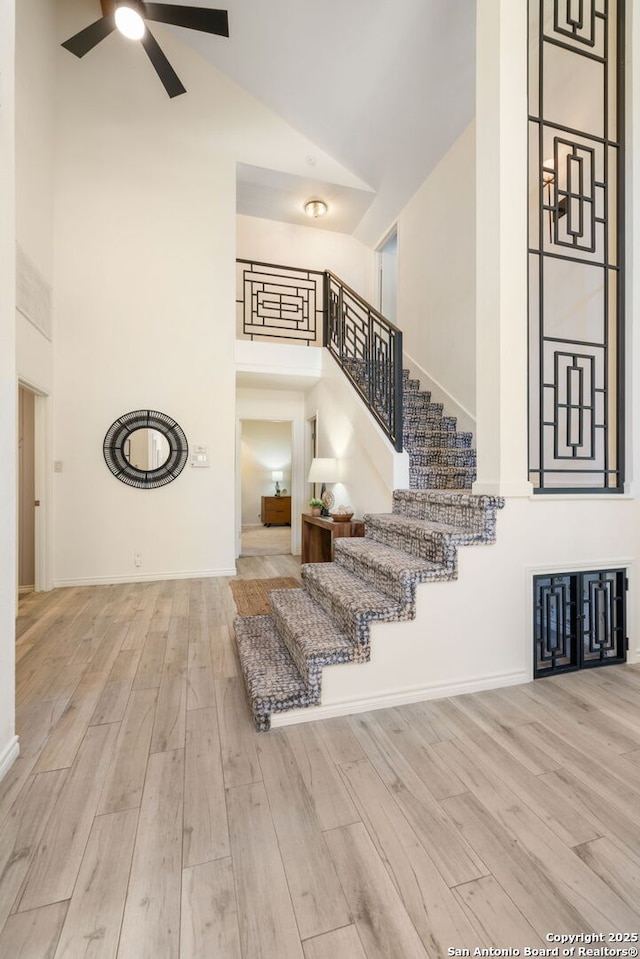 stairway with a ceiling fan, wood finished floors, baseboards, and high vaulted ceiling