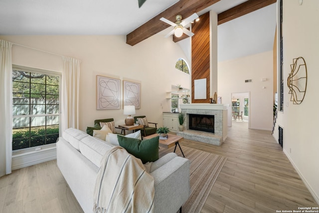 living area with wood finished floors, high vaulted ceiling, a fireplace with raised hearth, ceiling fan, and beamed ceiling