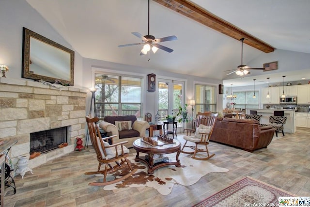 living area featuring light wood-type flooring, beam ceiling, high vaulted ceiling, a ceiling fan, and a stone fireplace