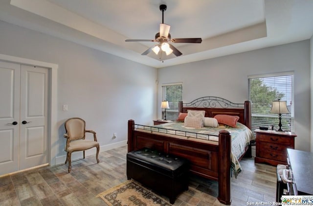 bedroom featuring a raised ceiling, a ceiling fan, baseboards, and light wood finished floors