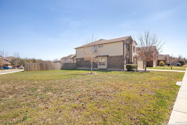 view of side of property with brick siding, a lawn, an attached garage, and fence