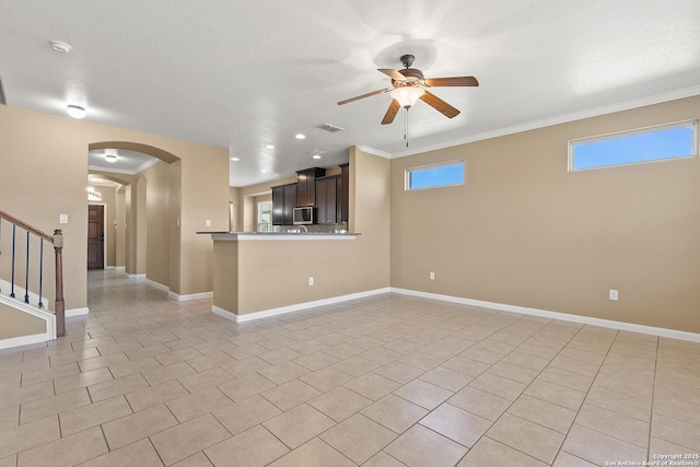 unfurnished living room featuring crown molding, baseboards, arched walkways, and ceiling fan