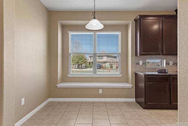 kitchen featuring light tile patterned floors, baseboards, hanging light fixtures, dark brown cabinetry, and tasteful backsplash