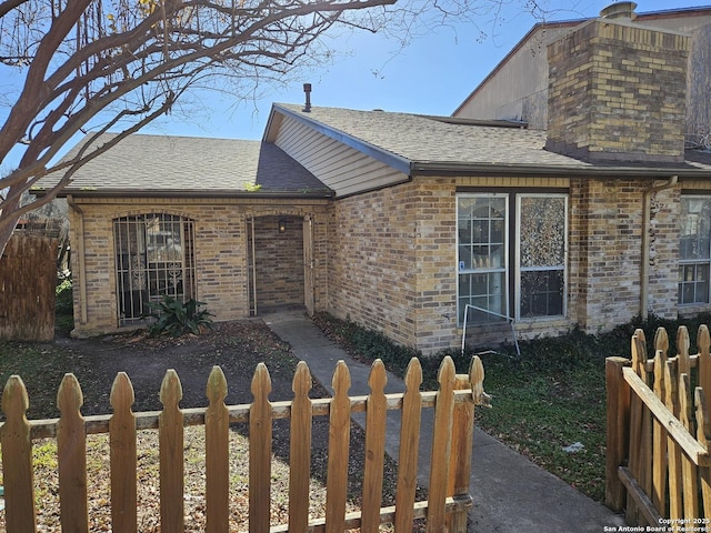 ranch-style home with a fenced front yard, a shingled roof, and brick siding