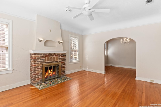 unfurnished living room with visible vents, ceiling fan, a fireplace, arched walkways, and wood-type flooring