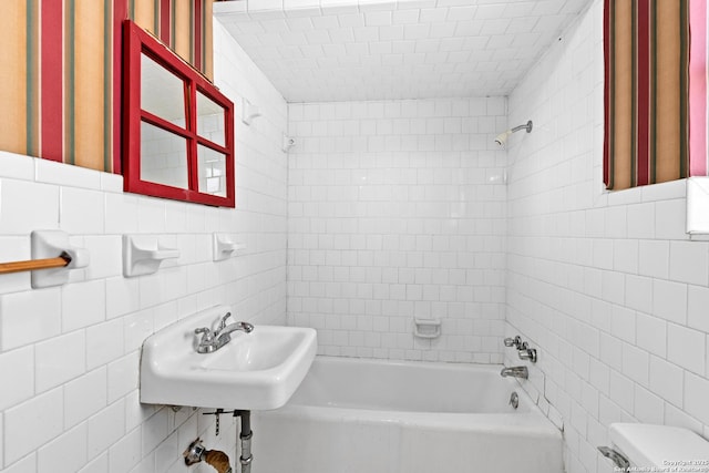 full bath featuring tile walls, shower / bathing tub combination, and a sink