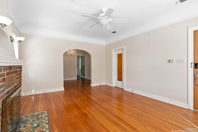 unfurnished living room with a brick fireplace, ornamental molding, hardwood / wood-style flooring, arched walkways, and a ceiling fan