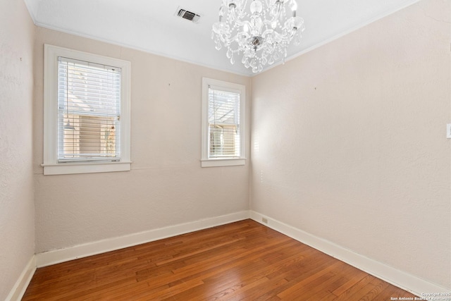 spare room featuring a notable chandelier, baseboards, wood-type flooring, and ornamental molding