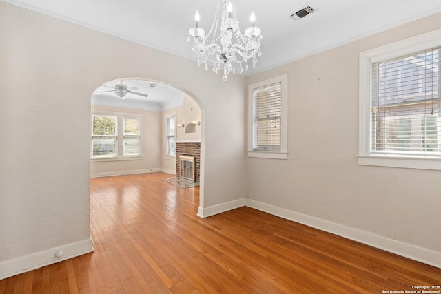 unfurnished dining area featuring visible vents, light wood-style flooring, arched walkways, baseboards, and a brick fireplace