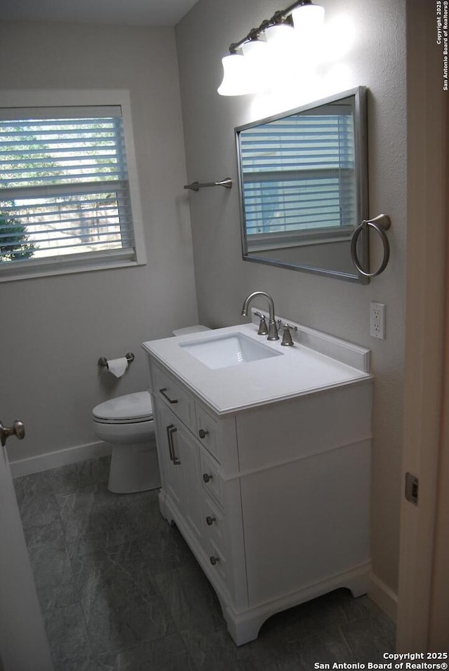 half bathroom with vanity, toilet, and baseboards