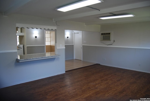 kitchen featuring a wall unit AC, beam ceiling, light stone counters, wood finished floors, and washer / clothes dryer