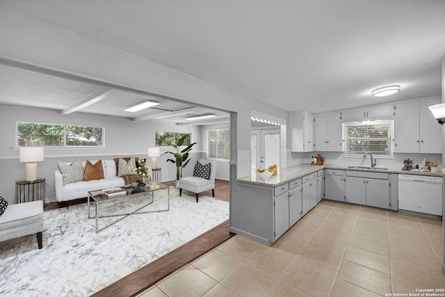 kitchen featuring light stone counters, light tile patterned floors, a sink, dishwasher, and tasteful backsplash