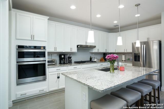 kitchen with a sink, under cabinet range hood, appliances with stainless steel finishes, a breakfast bar area, and white cabinets