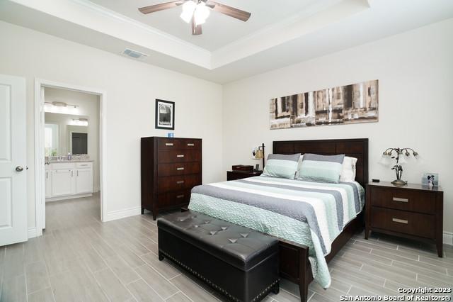 bedroom featuring wood finish floors, a tray ceiling, baseboards, and visible vents