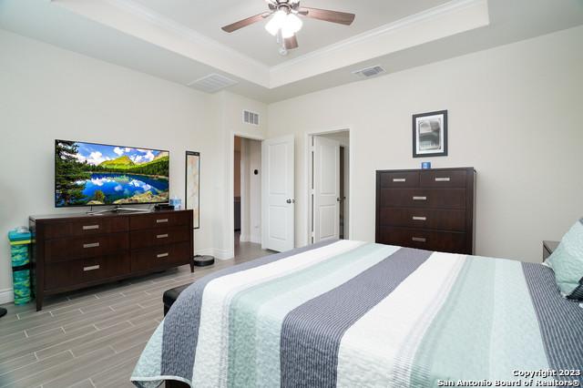 bedroom with visible vents, a tray ceiling, crown molding, baseboards, and wood tiled floor