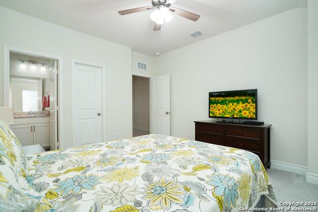 carpeted bedroom featuring ensuite bath, baseboards, visible vents, and ceiling fan