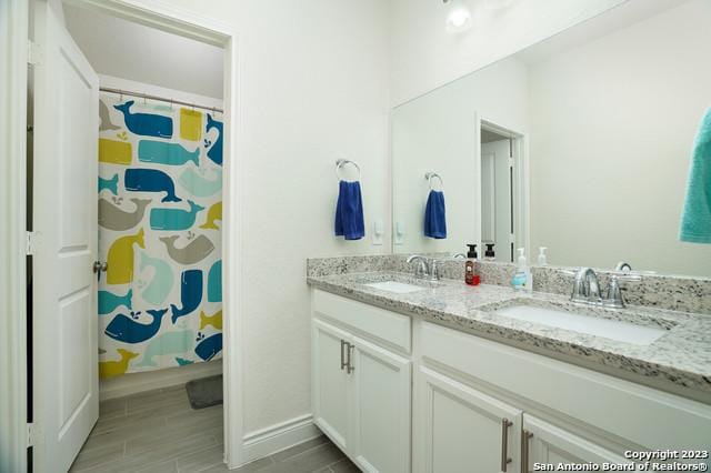 full bath with double vanity, baseboards, and a sink