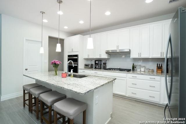 kitchen featuring an island with sink, a sink, stainless steel appliances, white cabinets, and under cabinet range hood